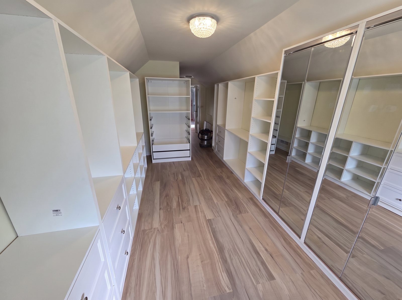 Long walk-in closet with white built-in shelving, drawers and mirrored doors
