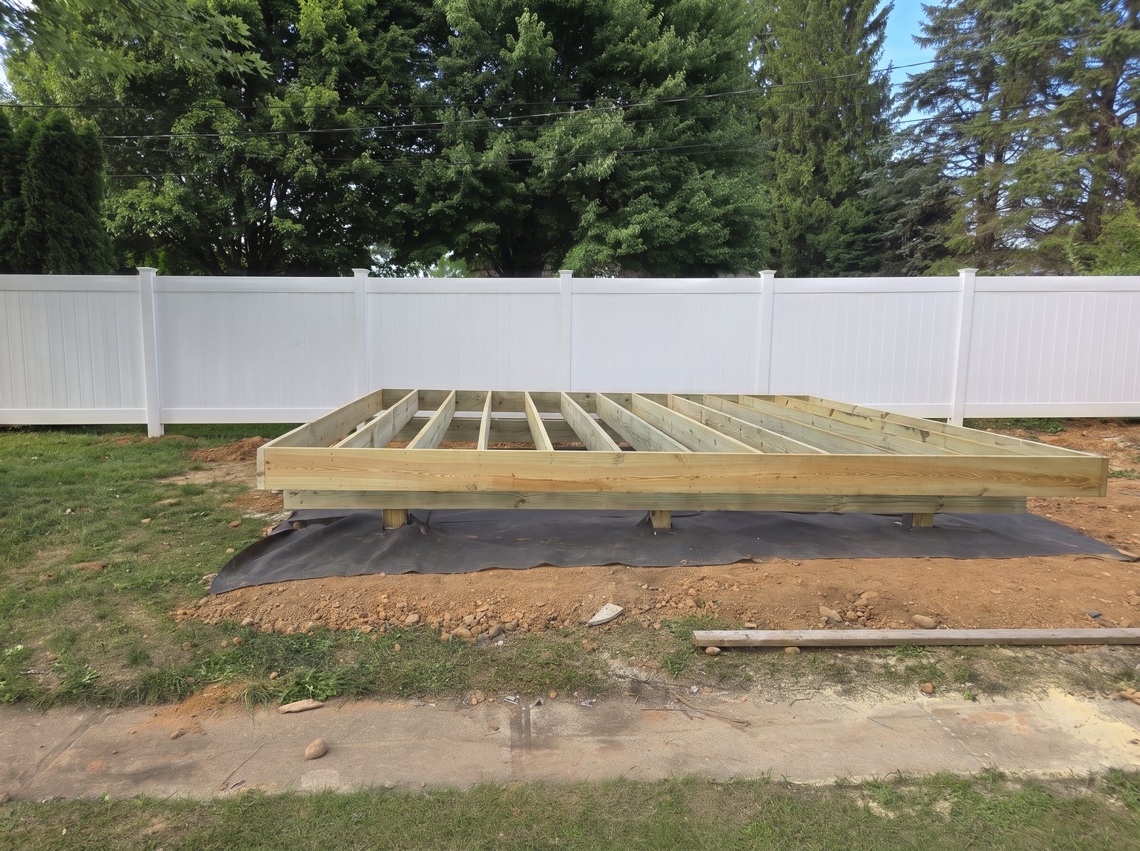 Pressure-treated deck frame on footings in a fenced backyard