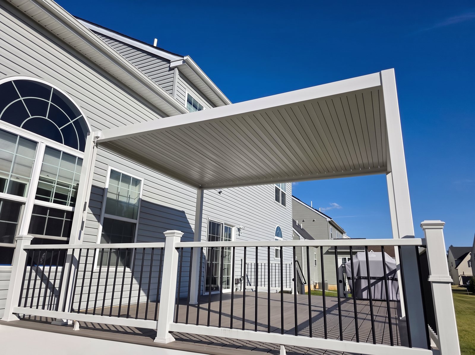 White louvered pergola on a deck next to a house